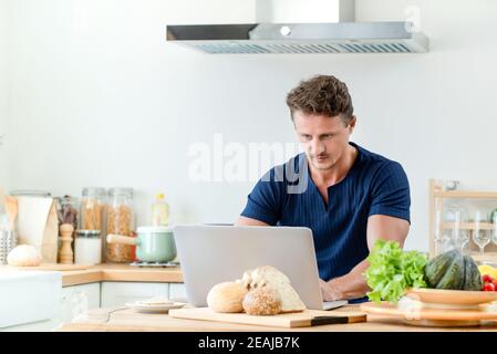 Bell'uomo che ha in linea chattare e lavorare da casa a. la cucina Foto Stock