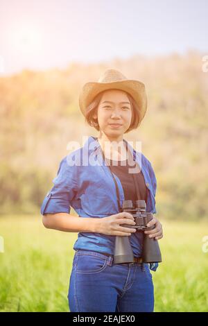 Donna usura hat e tenere premuto binocolo nel campo di erba Foto Stock