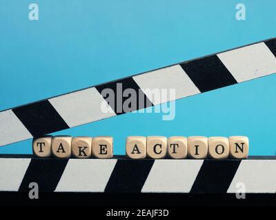 Piccoli blocchi di legno con l'iscrizione prendere azione su un clapperboard Foto Stock