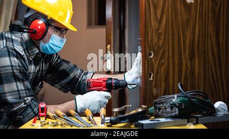 Il carpentiere al lavoro protegge il viso con la maschera chirurgica. Prevenzione di Covid-19. Foto Stock