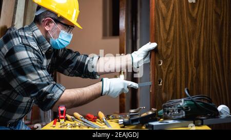 Il carpentiere al lavoro protegge il viso con la maschera chirurgica. Prevenzione di Covid-19. Foto Stock