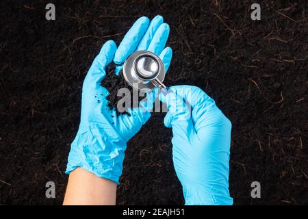 Mano di ricercatore che tiene uno stetoscopio su fertile suolo nero Foto Stock