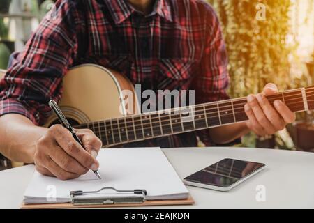 Un autore di canzoni che tiene una penna per comporre un brano. Musicista che suona la chitarra acustica. Musica dal vivo e concetto musicale astratto. Foto Stock