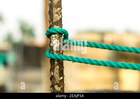 Una corda è legata in un nodo intorno a un palo di recinzione, corda legata attacco nodi su un palo di ferro arrugginito isolato da sfondo. Foto Stock