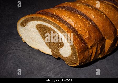 Insolito pane fresco a due colori su sfondo nero, foto in un tasto basso in luce dura, primo piano Foto Stock