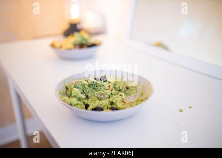 Ciotola di salsa di guacamole con olive su un tavolo bianco Foto Stock