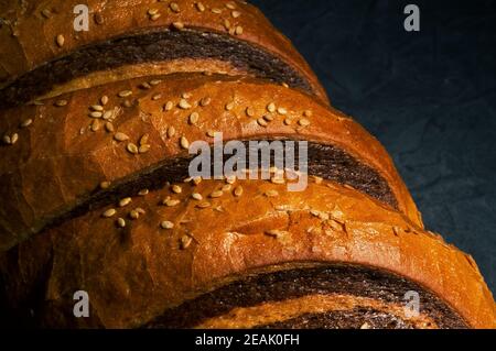 Insolito pane fresco a due colori su sfondo nero, foto in un tasto basso in luce dura, primo piano Foto Stock