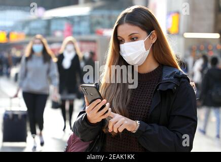 Studente universitario che cammina utilizzando il telefono cellulare indossando la maschera protezione come prevenzione per il coronavirus in aeroporto o stazione di città Foto Stock