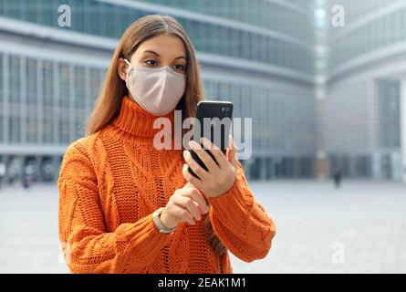 Giovane donna che indossa la maschera facciale utilizzando l'app per smartphone nella moderna strada della città. Spazio di copia. Foto Stock