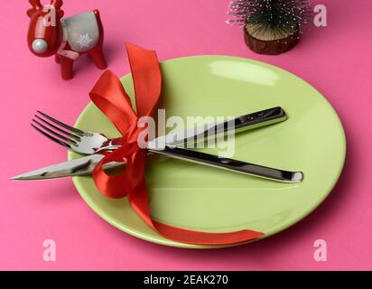 piastra rotonda verde e forcella e coltello in metallo legati con un nastro di seta rosso Foto Stock