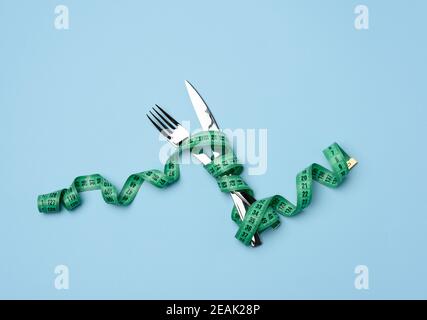 forcella e coltello avvolti in nastro di misurazione verde su blu sfondo Foto Stock