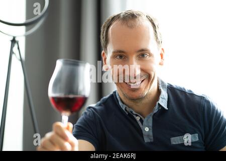 Uomo bere vino in videoconferenza Foto Stock