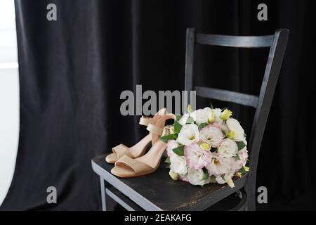 Bel bouquet di nozze con scarpe su una sedia nera sfondo nero Foto Stock