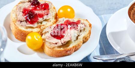 Toast con pate di carne e mostarda di frutta al mirtillo con pomodori ciliegini gialli e cop di caffè, primo piano. Concetto di colazione al mattino soleggiato. Lungo largo b Foto Stock