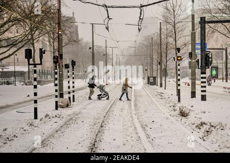Rotterdam, Paesi Bassi, 7 febbraio 2021: Coppia con il passeggino che attraversa le piste innevate del tram sul viale Coolsingel durante una bizzard Foto Stock