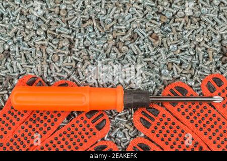 Il cacciavite e i guanti da lavoro giacciono su una pila di viti. Foto Stock