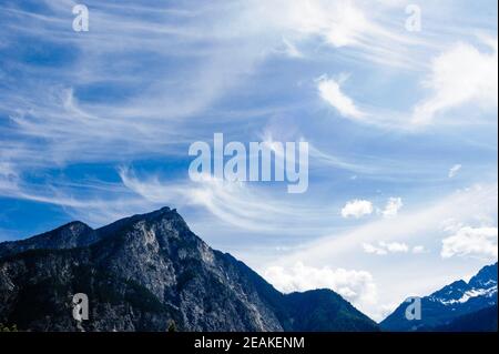 Le nuvole di Cirrus si diffondono in curve sopra le montagne. Foto Stock