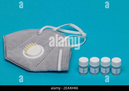 Concetto di trattamento del coronavirus. Primo piano di una maschera facciale N95 o di una semimaschera filtrante per particelle e di quattro fiale vaccino Covid-19 su sfondo blu. Spazio per il design. Foto Stock