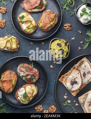 Bruschetta assortita con vari condimenti su piatti scuri su sfondo scuro. Bruschetta appetitosa. Cucina mediterranea. Vista dall'alto Foto Stock