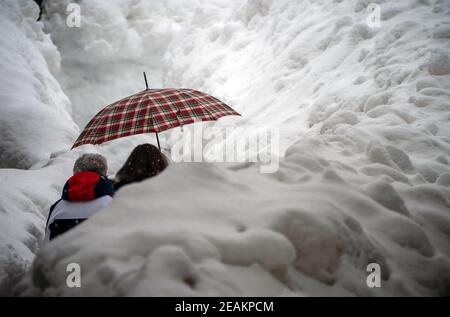 Cortina d'Ampezzo, Italia. 10 febbraio 2021, Italia, Cortina d'Ampezzo: Sci alpino, campionato del mondo: I pedoni sono al centro tra le masse di neve di Cortina. Dopo una forte nevicata, la giornata di gara è stata completamente annullata. La stazione sciistica è la sede delle Olimpiadi invernali 2026 che si terranno a Milano e Cortina d'Ampezzo. Foto: Michael Kappeler/dpa Credit: dpa Picture Alliance/Alamy Live News Foto Stock