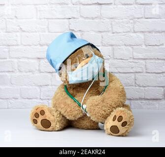 l'orsacchiotto marrone si trova in occhiali protettivi di plastica, una maschera medica monouso e un cappuccio blu Foto Stock