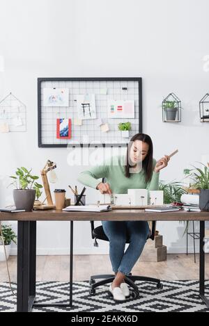 giovane architetto afroamericano che fa modelli di edifici durante il lavoro studio a casa Foto Stock