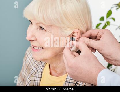 Audiologa che inserisce un apparecchio acustico intrauricolare a una paziente anziana, primo piano. Soluzione uditiva per anziani Foto Stock