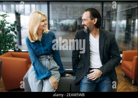 I colleghi che hanno avuto successo sono seduti sul divano in ufficio durante la pausa. Felice gente di affari di mezza età che ha una conversazione, che parla e discute il processo di lavoro, concetto di comunicazione Foto Stock