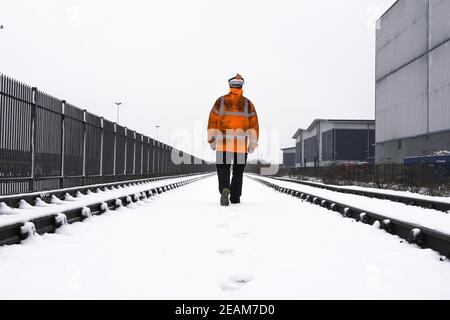 Vista posteriore di una guardia di sicurezza del lavoratore ferroviario che ispeziona il ferrovia durante la neve invernale pesante Foto Stock