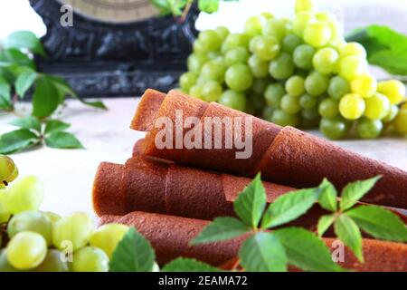 Pastilla dalle uve. Prodotto naturale senza conservanti. Cibo per vegetariani. Grappoli di uva su sfondo chiaro. Scale vintage sullo sfondo. Foto Stock