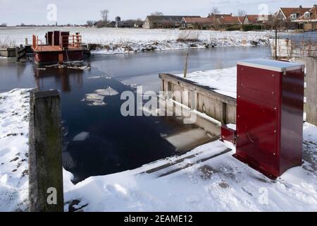 Bici e traghetto pedonale Ruterpolder Fr37 sopra il Geeuw in IJlst, Frisia nei Paesi Bassi in inverno con ghiaccio sul canale e lago Foto Stock