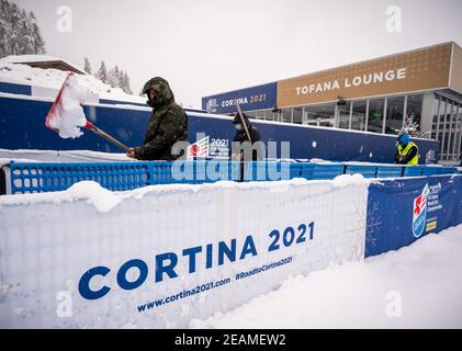 10 febbraio 2021, Italia, Cortina d'Ampezzo: Sci alpino: Coppa del mondo: Gli aiutanti scuotono la neve davanti alla tribuna vuota dei Campionati Mondiali di Sci. Dopo una forte nevicata, la giornata di gara è stata completamente annullata. La stazione sciistica è la sede delle Olimpiadi invernali 2026 che si terranno a Milano e Cortina d'Ampezzo. Foto: Michael Kappeler/dpa Foto Stock