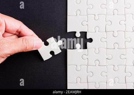 mano-tenendo ultimo pezzo di carta bianca jigsaw puzzle game ultimi pezzi mettere in posizione Foto Stock