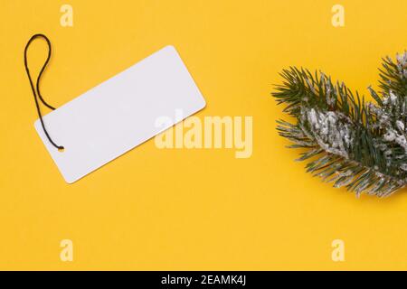 Modello per la vendita di natale. Un cartellino bianco e un ramo di abete su sfondo giallo. Concetto di vendita invernale o del Black Friday. Spazio vuoto per la progettazione. Foto Stock