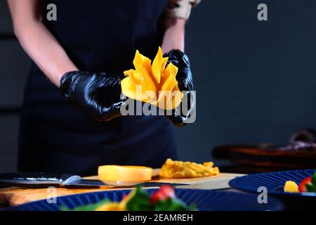 Cuoco taglia un mango maturo. Preparazione di insalata di mango e polpo. Persona irriconoscibile. Foto all'interno. Foto Stock