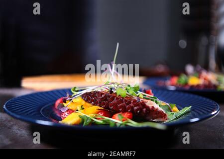 Insalata di polpo con mango e fragole su un piatto blu. Microvreens in un'insalata con un polpo. Primo piano. Foto Stock