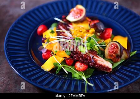 Insalata di polpo con mango e fragole su un piatto blu. Foto senza persone. Concetto di cucina. Foto Stock