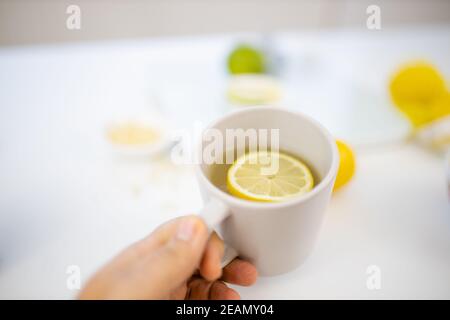Mano femminile che tiene una tazza di tè al limone sopra i lime e limoni Foto Stock