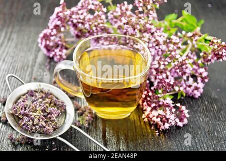 Tè di origano in tazza con succhietto su tavola di legno Foto Stock