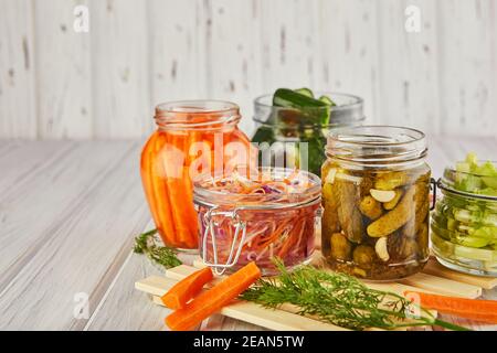 Primo piano di carote fermentate, crauti, cetrioli in vasi di vetro su un tavolo da cucina in legno Foto Stock