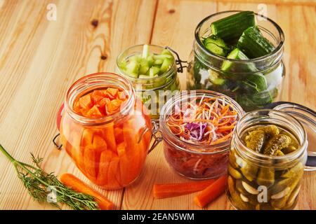 Primo piano di carote fermentate, crauti, cetrioli in vasi di vetro su un tavolo da cucina in legno Foto Stock