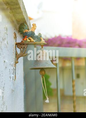 Piccola campana di ferro con gallo colorate al di fuori della casa. Foto Stock