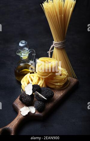 Tartufi neri e pasta sotto forma di nidi su una tavola di legno. Gli spaghetti sono legati con una corda. Olio d'oliva in una bottiglia di vetro. Antiossidante naturale. Il fungo più costoso. Sfondo scuro.foto verticale. Foto Stock