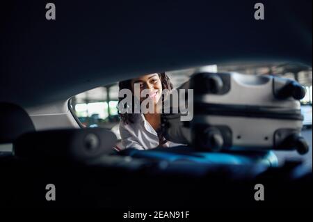 Donna sorridente mette valigie in macchina, parcheggio Foto Stock