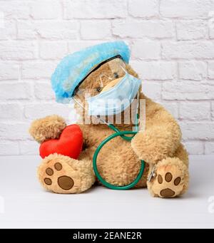 l'orso di teddy si trova in occhiali protettivi di plastica, una maschera medica usa e getta e un cappuccio blu Foto Stock