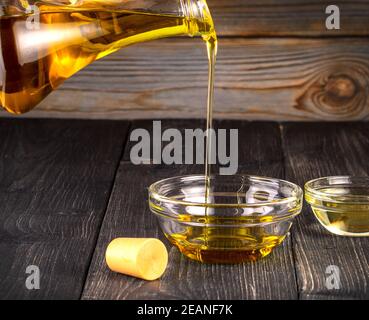 Versando l'olio di cottura una piccola tazza di vetro sul legno vecchio tabella Foto Stock