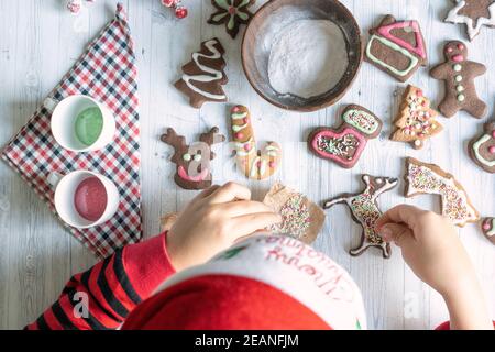 Carino bambino con cappello di Santa che decorano i biscotti fatti in casa di pan di zenzero a Natale visto dall'alto, Italia, Europa Foto Stock