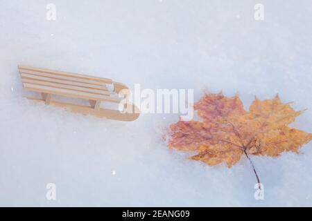 Slitte decorative nella neve e una foglia d'acero. Inverno, vacanza, vacanza concetto. Foto di alta qualità Foto Stock