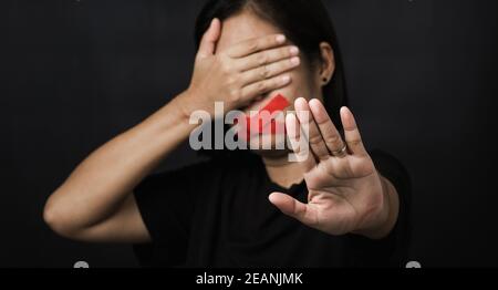 Donna che avvolge la bocca con nastro adesivo e mostra il segnale di arresto della mano abuso di violenza Foto Stock