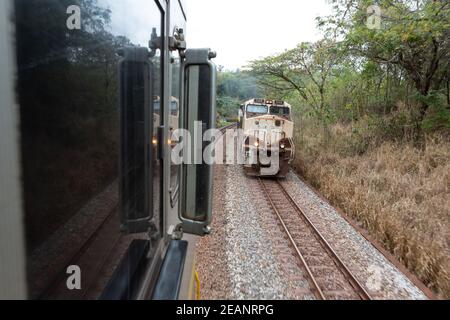 Vista del ferro minerale vecchio treno che corre sulle piste ferroviarie visto dalla finestra della locomotiva il giorno nuvoloso, Minas Gerais, Brasile. Concetto di industria. Foto Stock